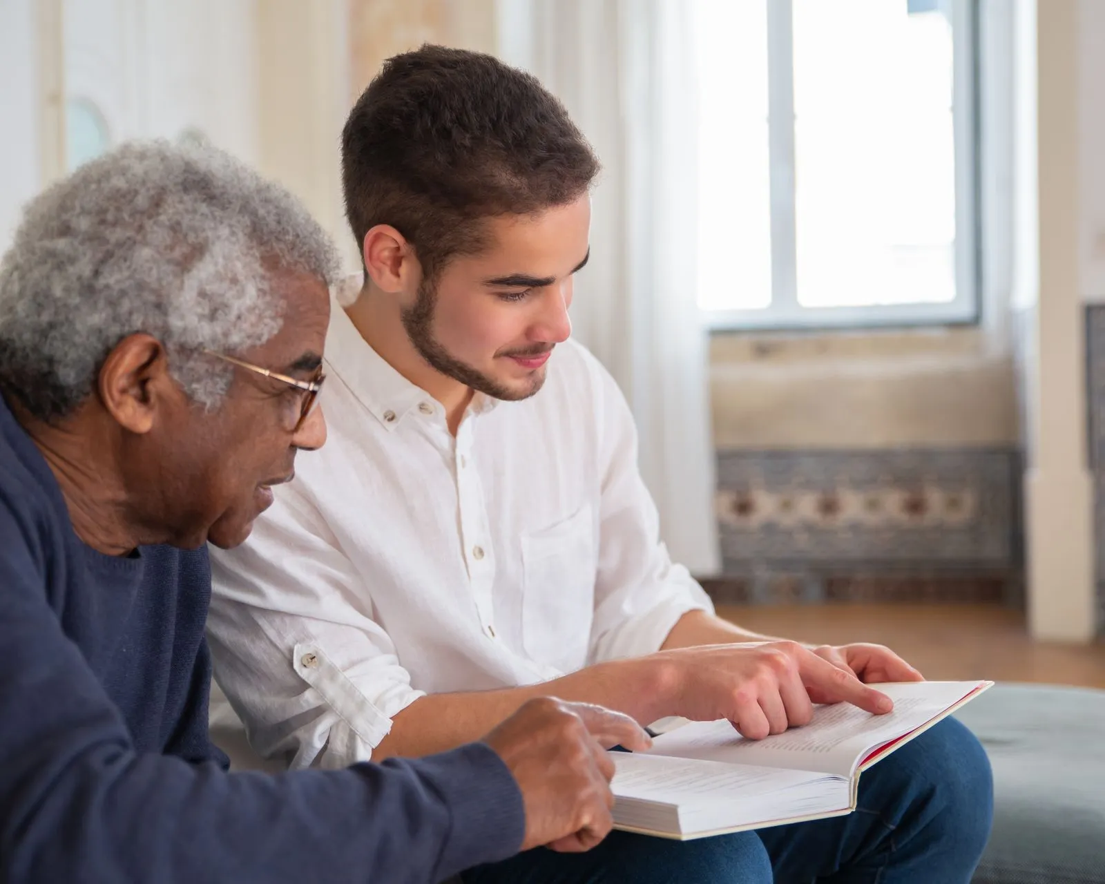 Younger adult and older adult reading a book together at home