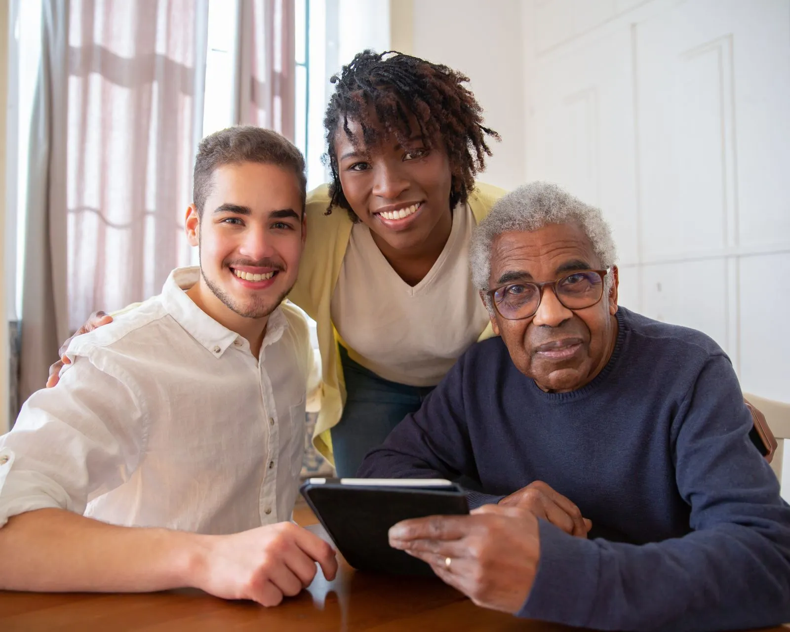 Family members sitting with an older adult at a table reviewing a tablet together
