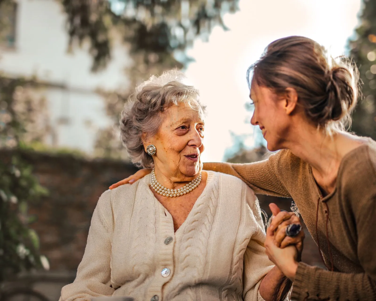 Adult daughter holding hands with her mother outdoors in soft natural light